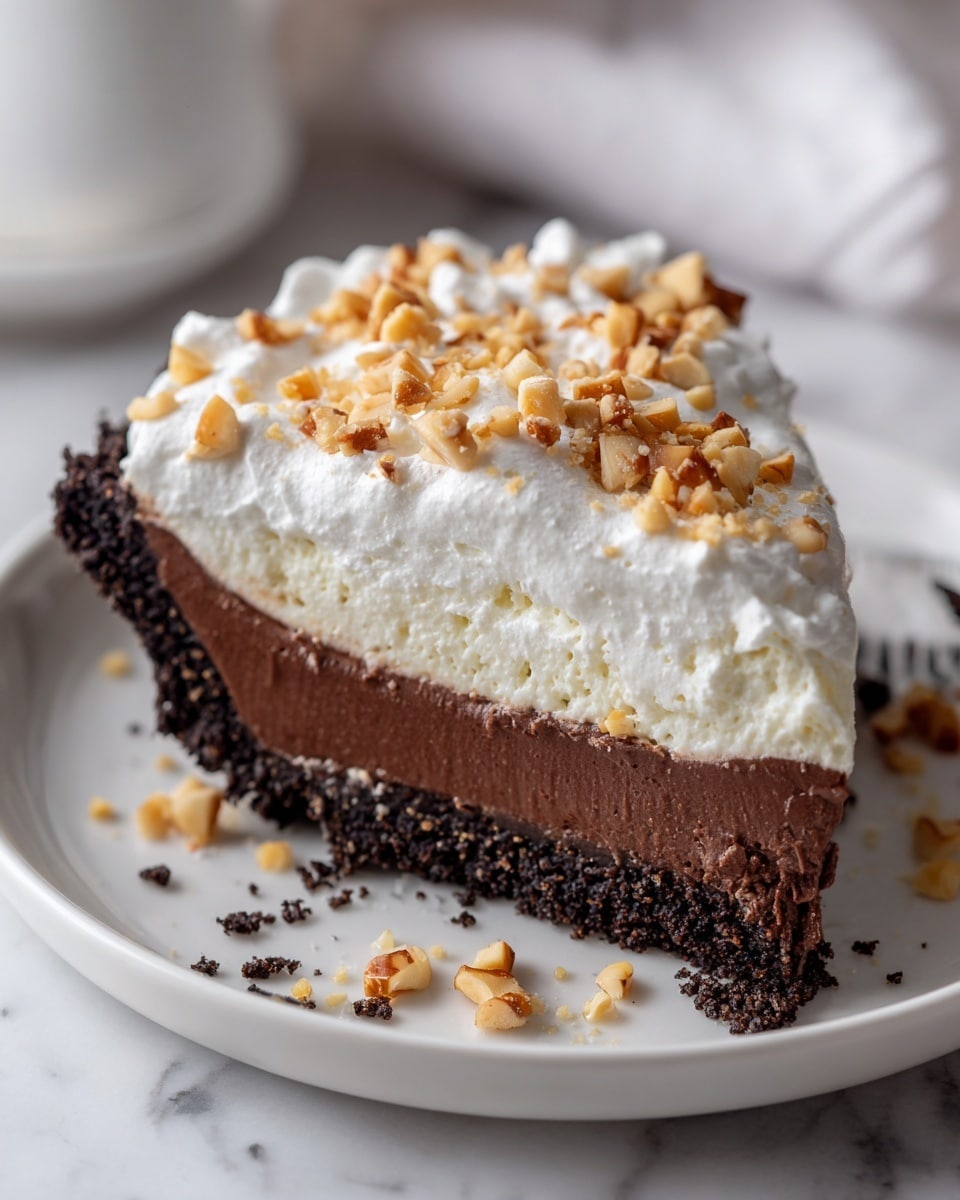 A slice of pie is shown on a white plate with crumbs around it, sitting on a white marbled surface. The pie has three main layers: the bottom crust is dark brown and crumbly, the middle layer is thick and smooth chocolate filling in a medium brown shade, and the top layer is fluffy white whipped cream, topped with small pieces of chopped nuts. The slice looks rich and creamy with clear separation between each layer. Photo taken with an iphone --ar 4:5 --v 7