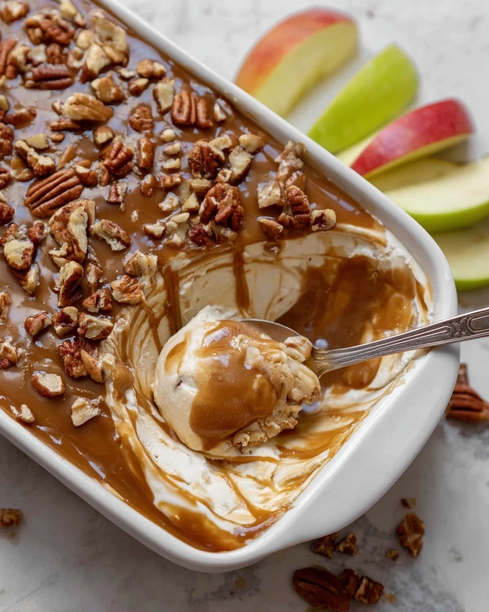 The image shows a white rectangular dish filled with a creamy dessert that has three visible layers: a thick creamy white layer at the bottom, a smooth brown caramel layer on top, and chopped pecans sprinkled all over the caramel layer. A spoon is scooping into the dessert, mixing some of the creamy base with the caramel and nuts, creating a swirled texture. Next to the dish, there are apple slices in green and red colors resting on a white marbled surface. Photo taken with an iphone --ar 4:5 --v 7