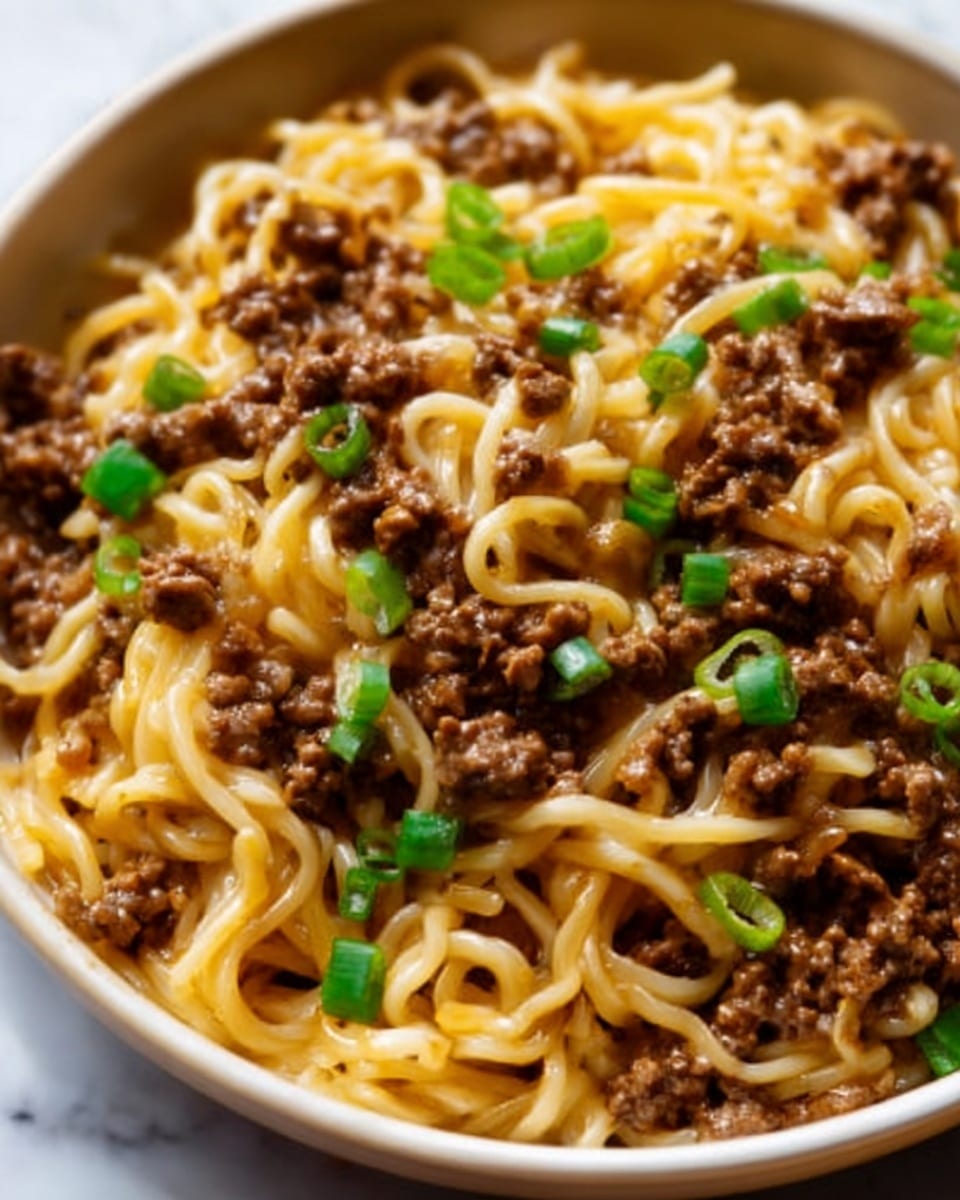 The image shows a close-up of a dish with thick yellow noodles topped with small pieces of cooked ground beef that have a slightly shiny texture from sauce. On top of the meat and noodles, there are small chopped green onions scattered evenly, adding a touch of bright green color. The food is served on a white plate, placed on a white marbled surface. The photo taken with an iphone --ar 4:5 --v 7