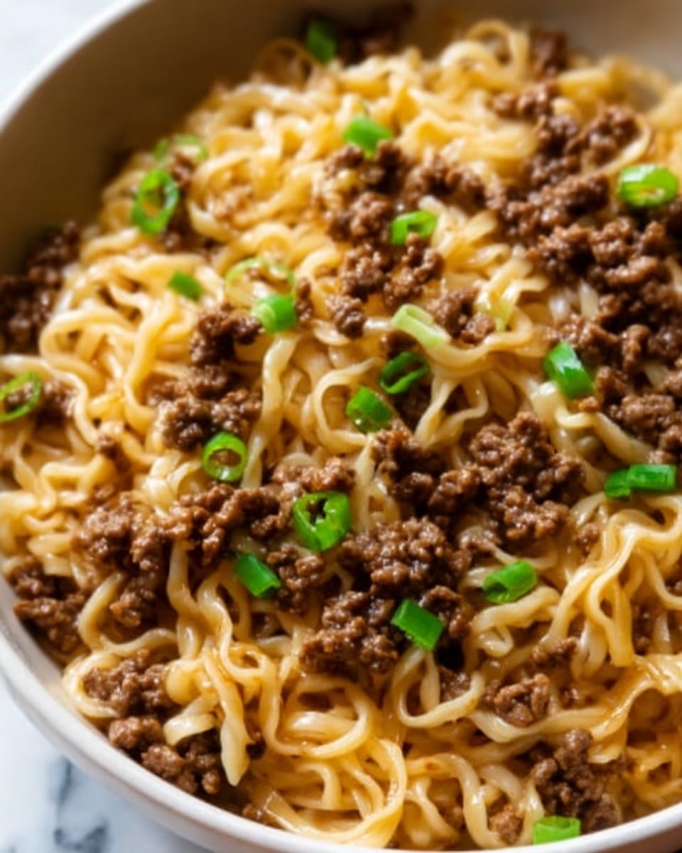 The image shows a close-up of a white bowl filled with cooked noodles mixed with small pieces of browned ground beef scattered evenly on top. The noodles are slightly shiny and light yellow, with a soft texture, while the ground beef is dark brown and crumbly. There are small pieces of green onions sprinkled across the surface, adding a touch of bright green color. The bowl sits on a white marbled surface, and the overall look is rich and savory. Photo taken with an iphone --ar 4:5 --v 7