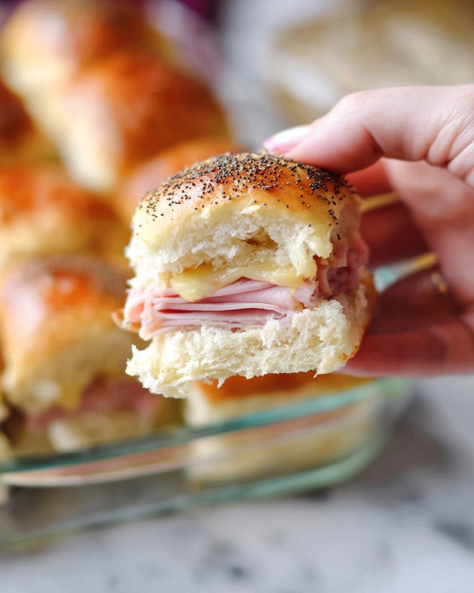 A close-up of a small sandwich being held by a woman's hand, showing three layers: a golden brown top bun sprinkled with black poppy seeds, a middle layer of folded pink ham, and a bottom layer of soft, light-colored bread. The sandwich has a smooth and slightly shiny texture on the top bun, with a light, fluffy inside. In the background, there is a clear glass dish with more sandwiches on a white marbled surface. photo taken with an iphone --ar 4:5 --v 7