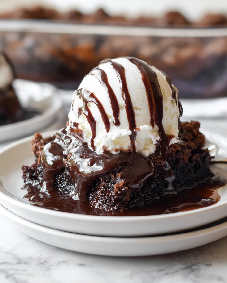 A close-up of a dessert on a stack of two white plates showing three distinct layers: the bottom layer is crumbly dark chocolate cake, the middle layer is a rich, glossy dark chocolate sauce oozing over the cake, and the top layer is a round scoop of white vanilla ice cream drizzled with thin stripes of dark chocolate syrup. The background shows a blurred glass baking dish with more dessert inside, all placed on a white marbled surface. photo taken with an iphone --ar 4:5 --v 7