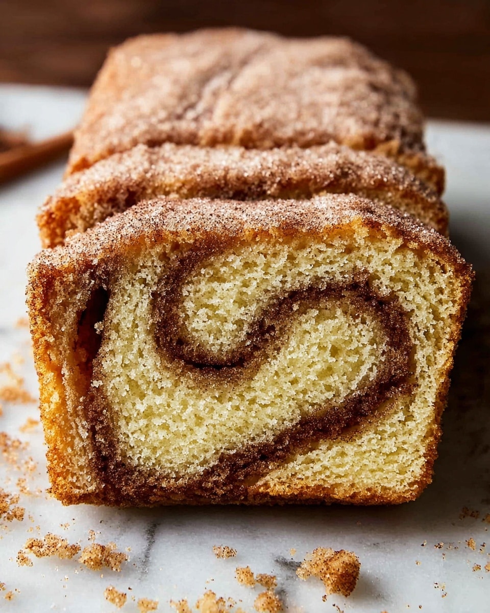The image shows a close-up of a cinnamon swirl cake loaf. The cake has about four visible layers with a soft, light yellow sponge texture. A thin, dark brown cinnamon sugar swirl wraps through the middle of the cake in a spiral pattern. The top layer is covered with a light dusting of granulated sugar mixed with cinnamon, giving it a slightly rough texture. Crumbs and sugar particles are scattered around the base of the loaf on a white marbled surface. Photo taken with an iphone --ar 4:5 --v 7