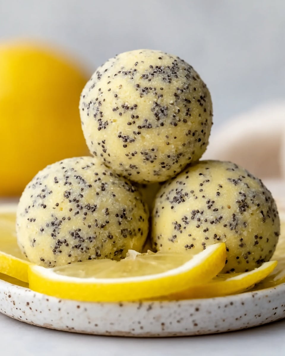 The image shows three round, light-colored dessert balls covered in small black seeds, stacked neatly on a white plate with a slightly speckled edge. The balls have a creamy, slightly grainy texture with visible bits of yellow zest. In the background, there is a lemon wedge, adding a bright yellow contrast to the neutral colors of the dessert. The whole setting is on a white marbled surface, giving a clean and simple look. photo taken with an iphone --ar 4:5 --v 7